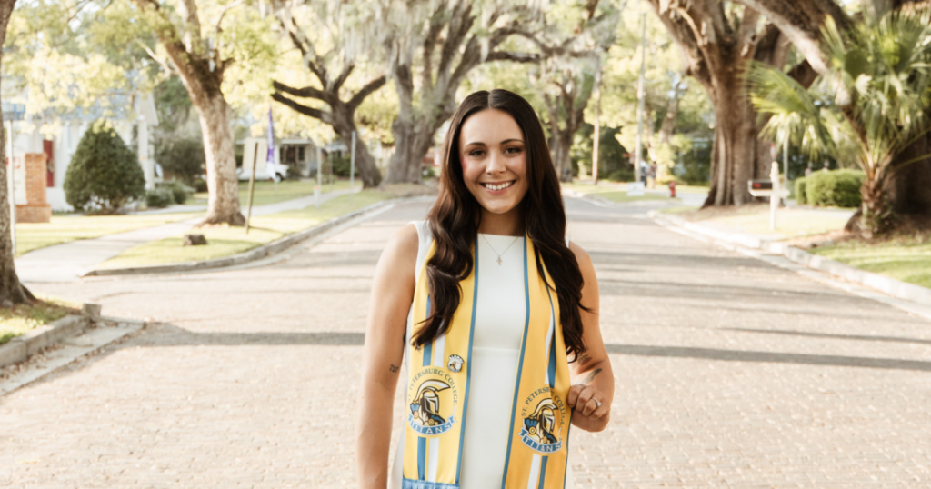 Julia stands outside wearing a yellow St. Petersburg College graduation stole.